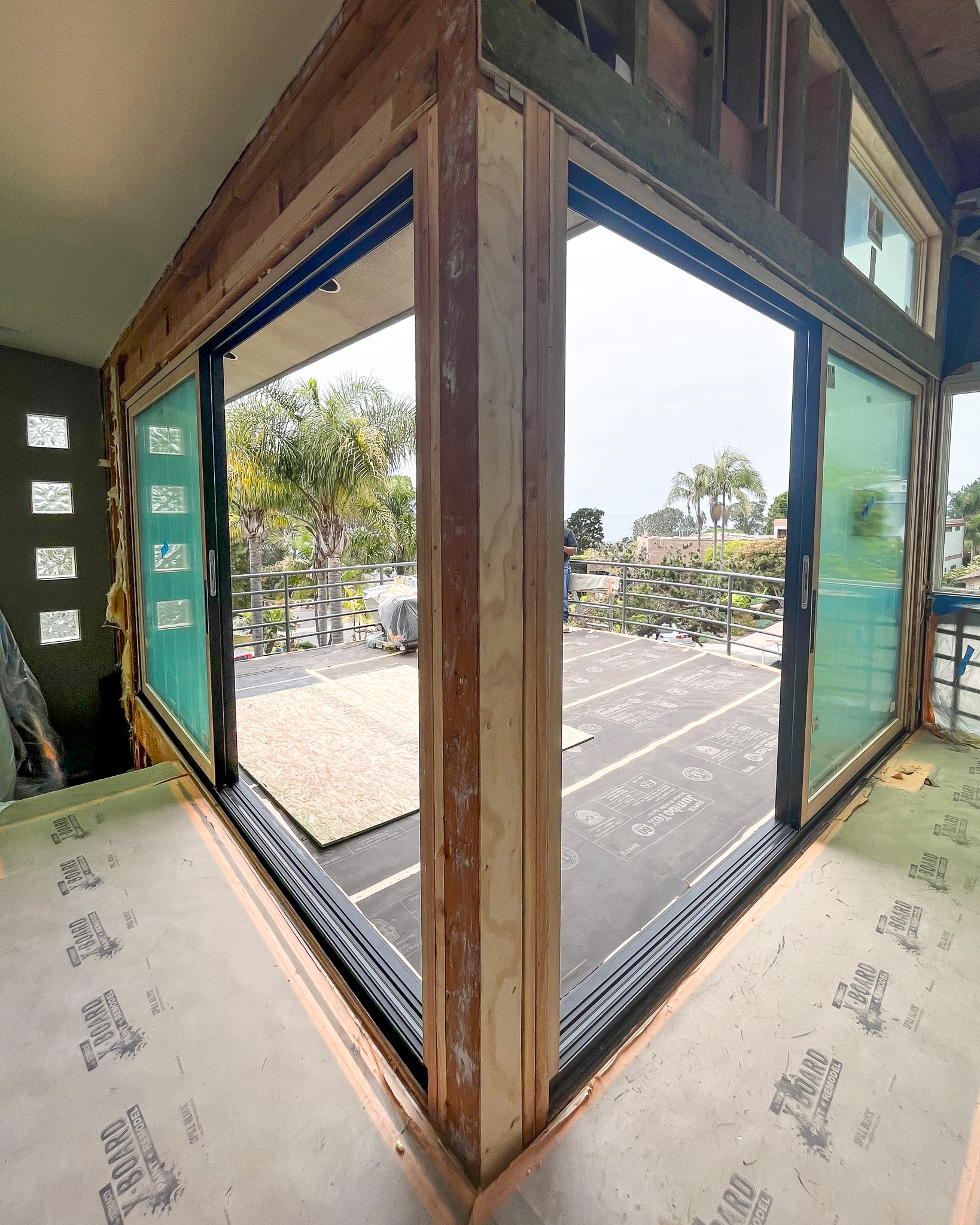 View from inside a room under construction with open glass folding doors leading to a balcony overlooking a garden.