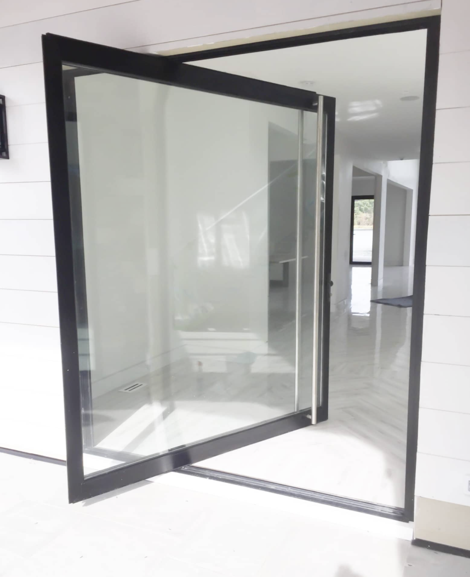 Glass door with a black frame partially open, leading to a hallway with white walls and glossy floor tiles.