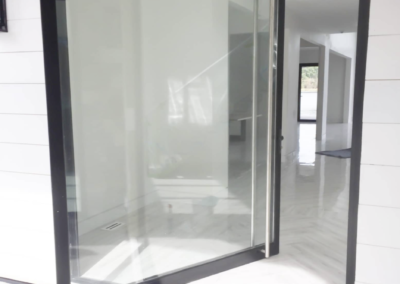 A glass door framed in black is partially open, leading into a bright, white corridor with visible sunlight reflecting off the shiny floor.