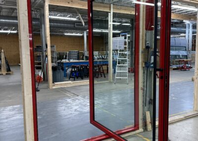 A large red-framed glass door is partially opened in a workshop with various tools, equipment, and workbenches visible in the background.